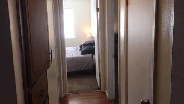 A narrow hallway leading to a bedroom with a bed, a nightstand, and a window. - Fully furnished two bedroom apartment (Lawton)