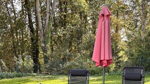 A garden with two black chairs and a red umbrella, surrounded by green plants and trees. - Côté Jardin" self-catering cottage, Contrexéville spa resort (Contrexéville)