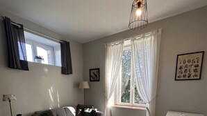 A modern living room with a grey sofa, a wooden coffee table, a white side table, a white desk, and a hanging light fixture. - Côté Jardin" self-catering cottage, Contrexéville spa resort (Contrexéville)