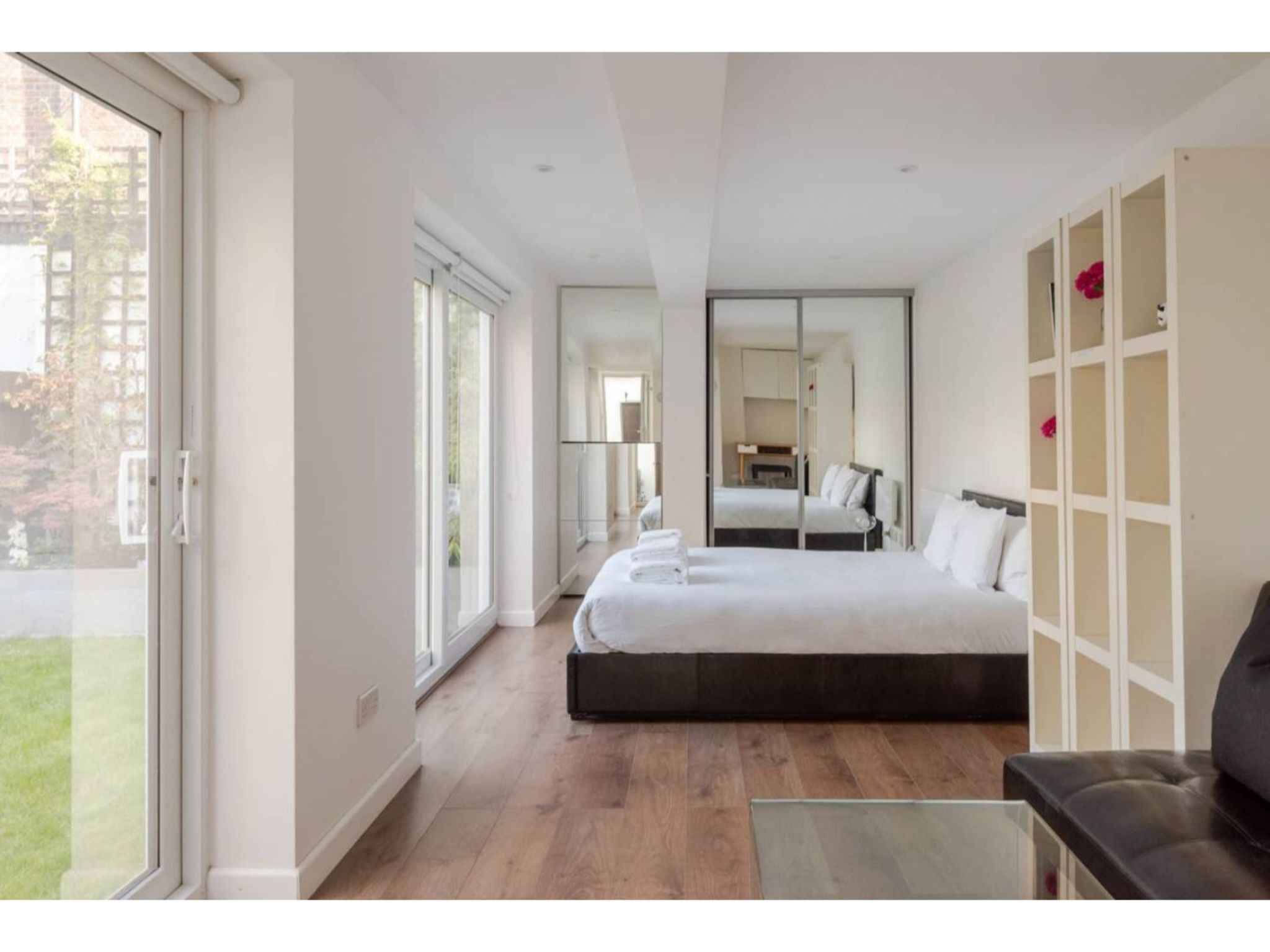 Ein modernes Hotelzimmer mit einem großen Bett, einem Glastisch und Blick ins Freie.