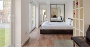 A modern hotel room with a large bed, a glass coffee table, and a view of the outdoors. - King's Cross Garden Flat - Pass the Keys (London)