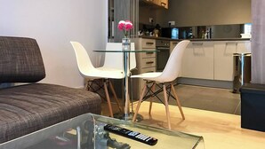 A modern living room with a glass coffee table, two white chairs, a brown sofa, and a kitchen in the background. - King's Cross Garden Flat - Pass the Keys (London)