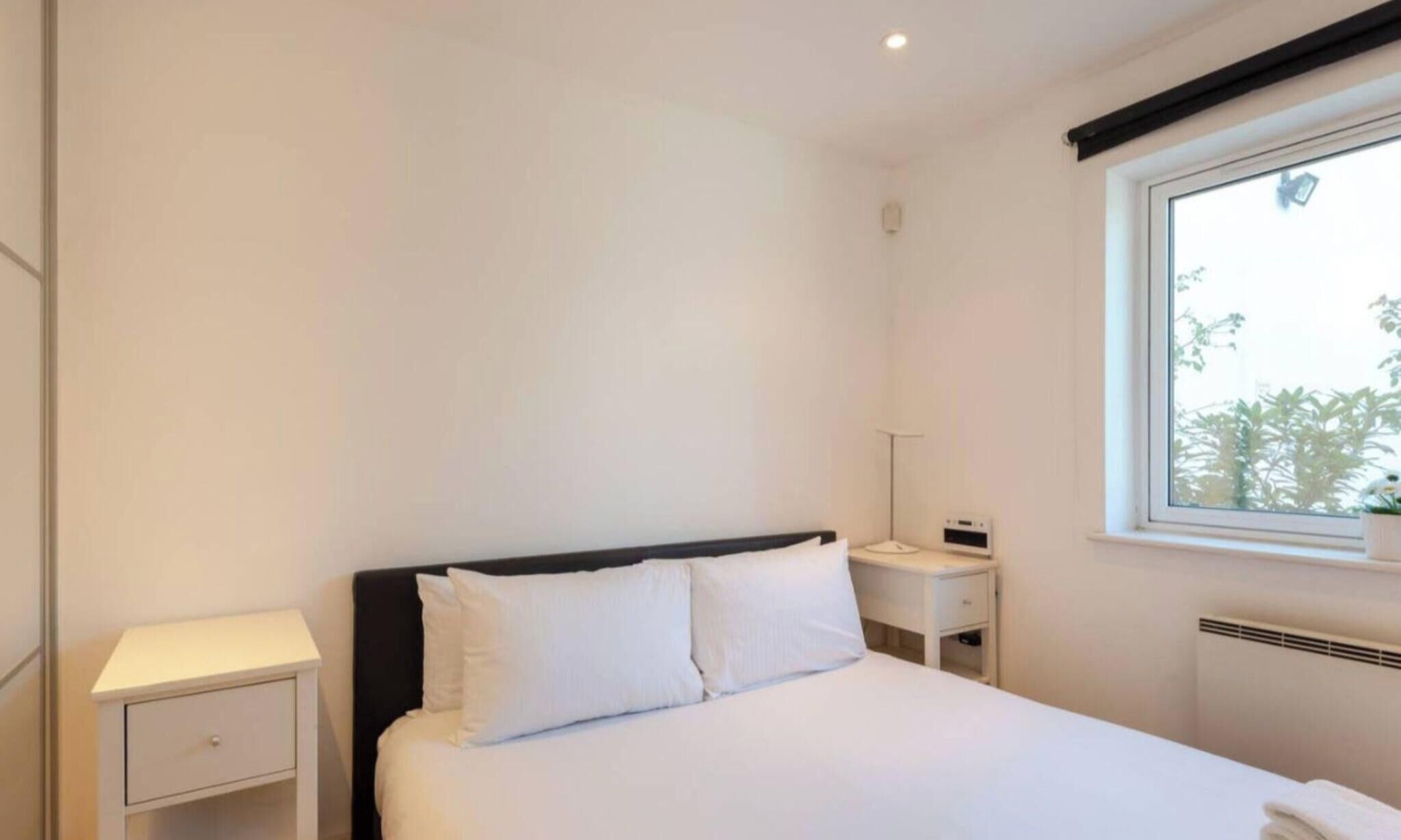 Habitació d'hotel minimalista amb un llit individual, una taula de nit i una finestra que ofereix vistes a la vegetació.