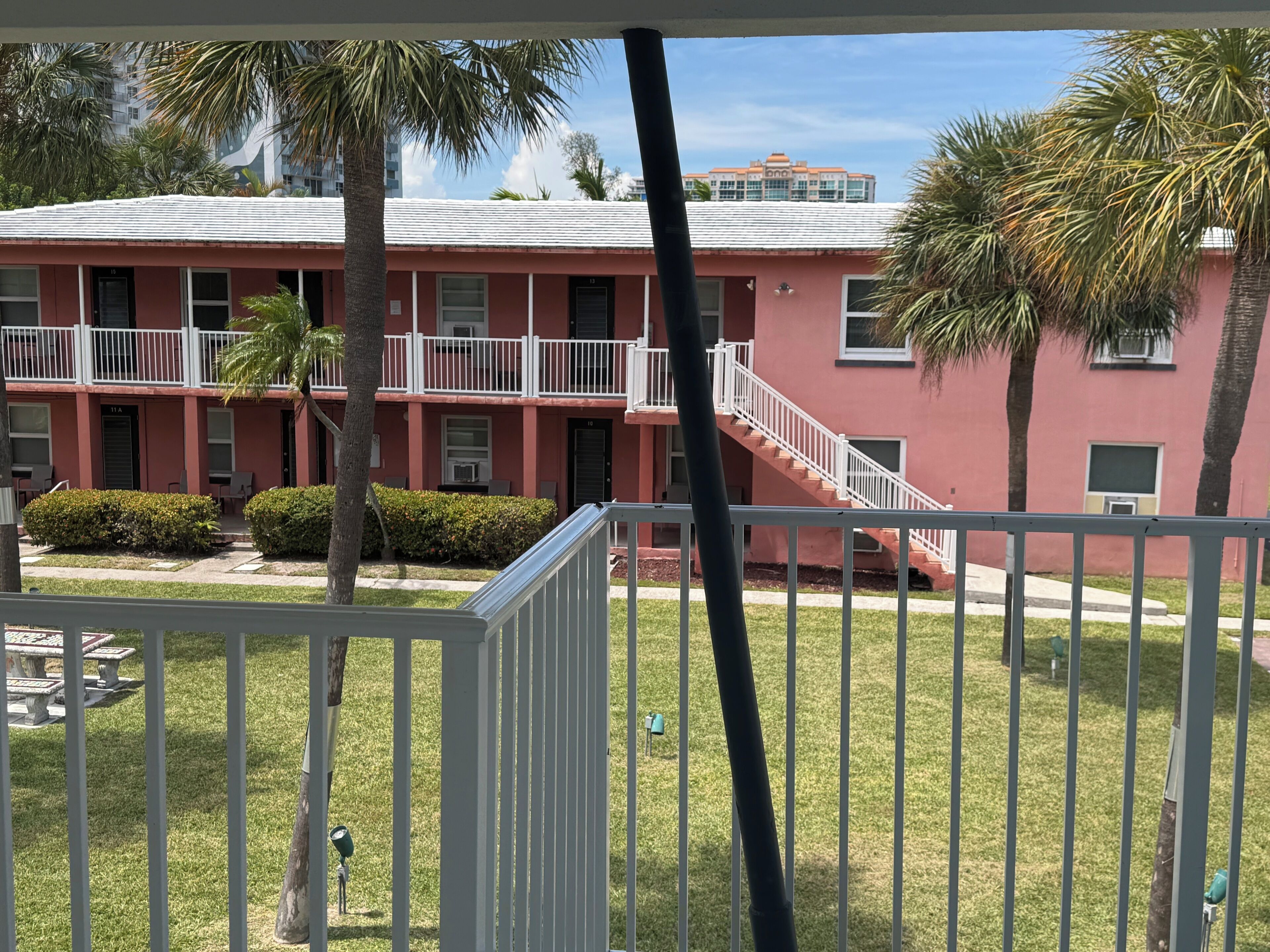 A pink building with balconies, a staircase, and a lawn with palm trees.