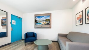 A modern hotel lobby with a blue door, a round table, a blue armchair, a gray sofa, and a framed picture of a pool on the wall. - Rolo Beach Hotel (Fort Lauderdale)