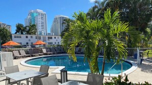 A poolside area with lounge chairs, a table, and a palm tree. - Rolo Beach Hotel (Fort Lauderdale)