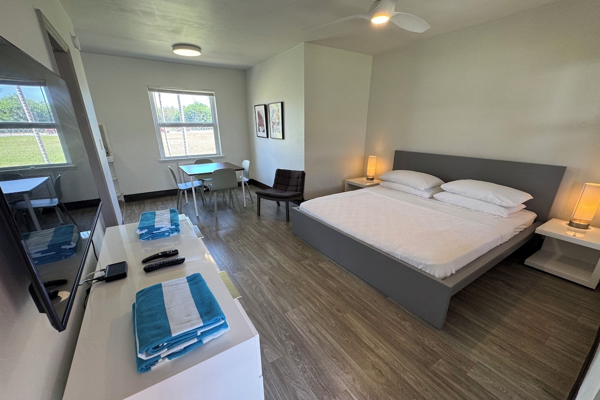 A hotel room with a bed, bedside tables, a desk, a chair, a mirror, and a window.