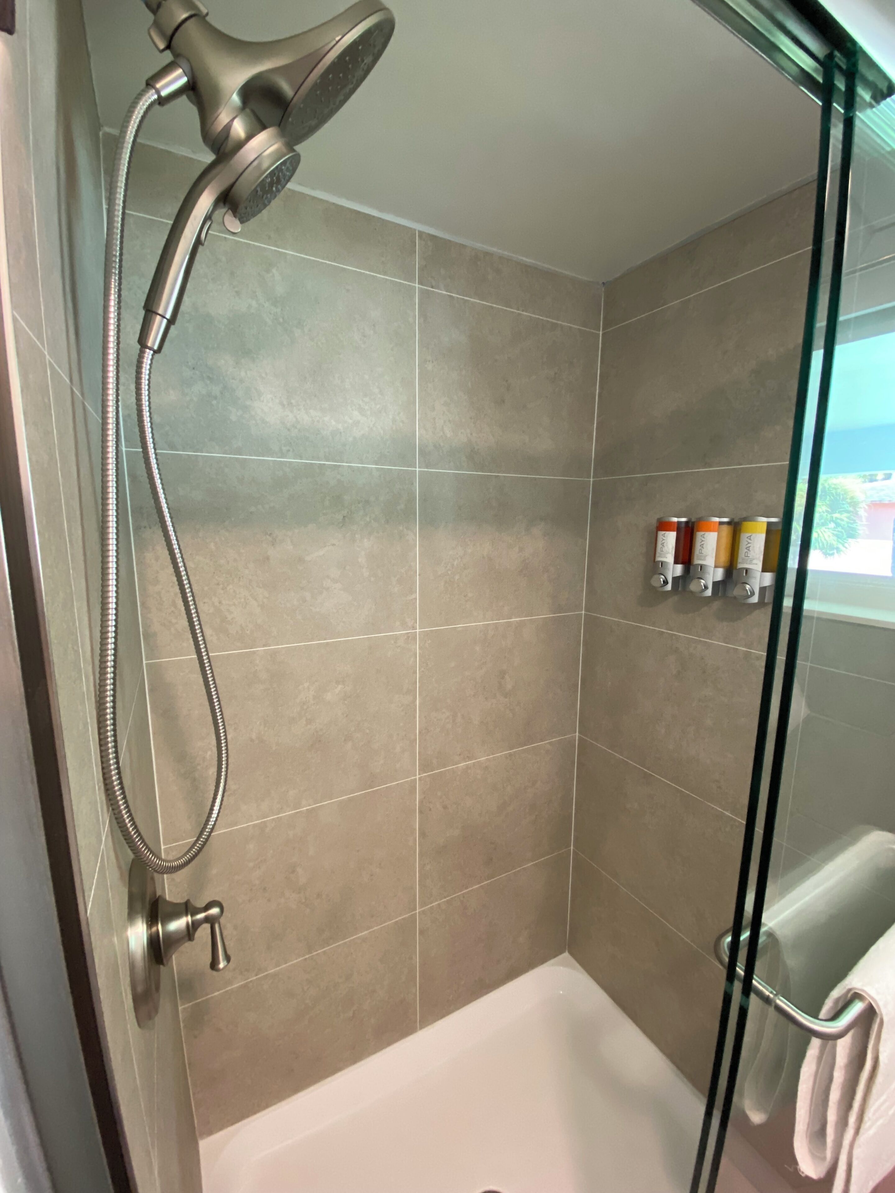 A shower with a handheld showerhead, a glass door, and a tiled wall.