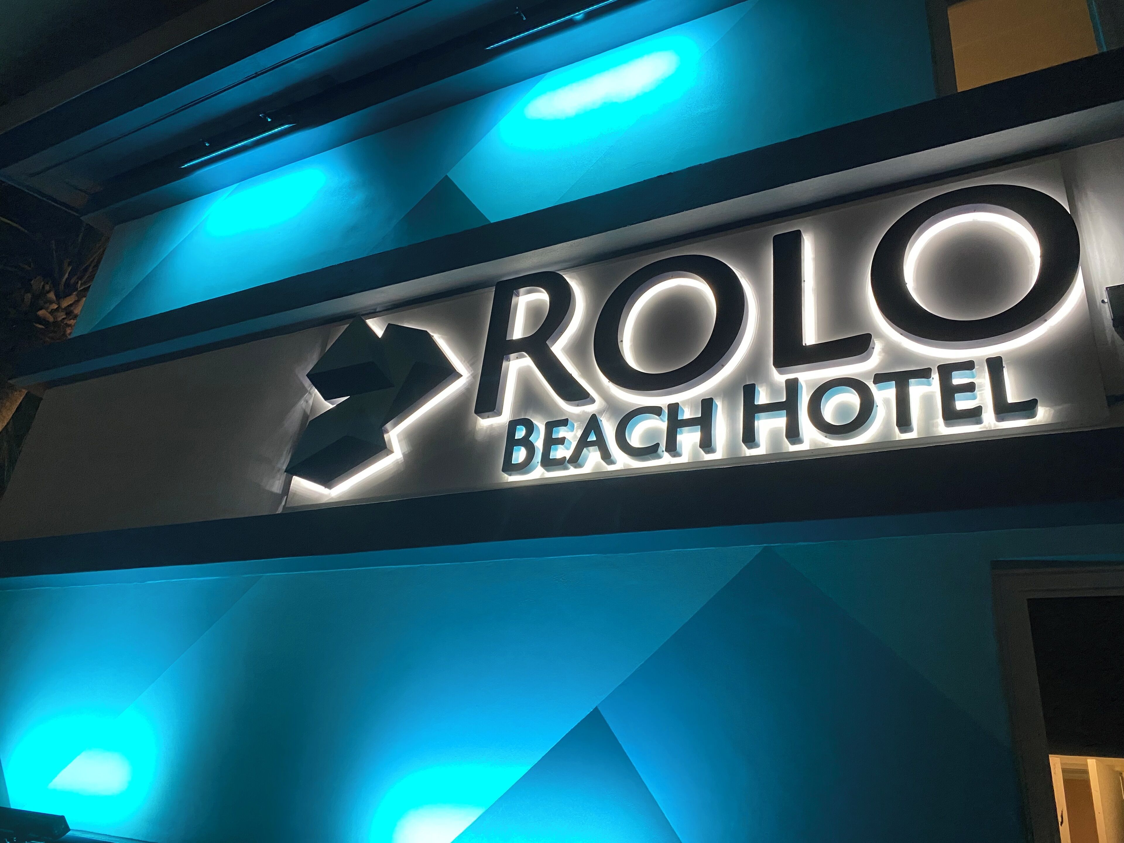 Letrero del Hotel Rolo Beach con letras iluminadas y un diseño de luces geométrico.