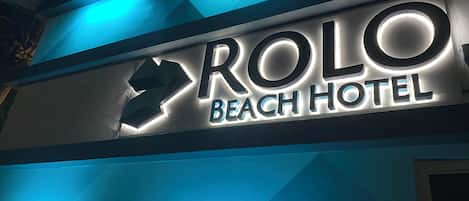 Letrero del Hotel Rolo Beach con letras iluminadas y un diseño de luces geométrico.