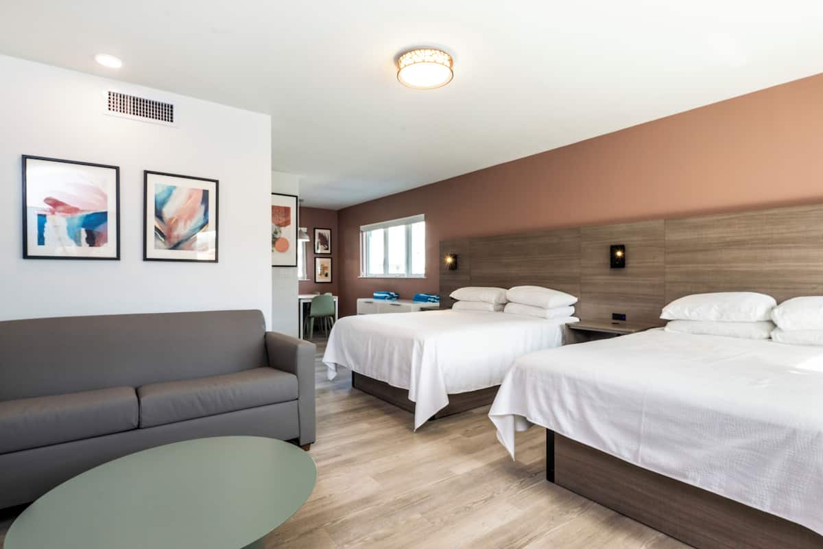 A hotel room with two beds, a sofa, a desk, and artwork on the walls.