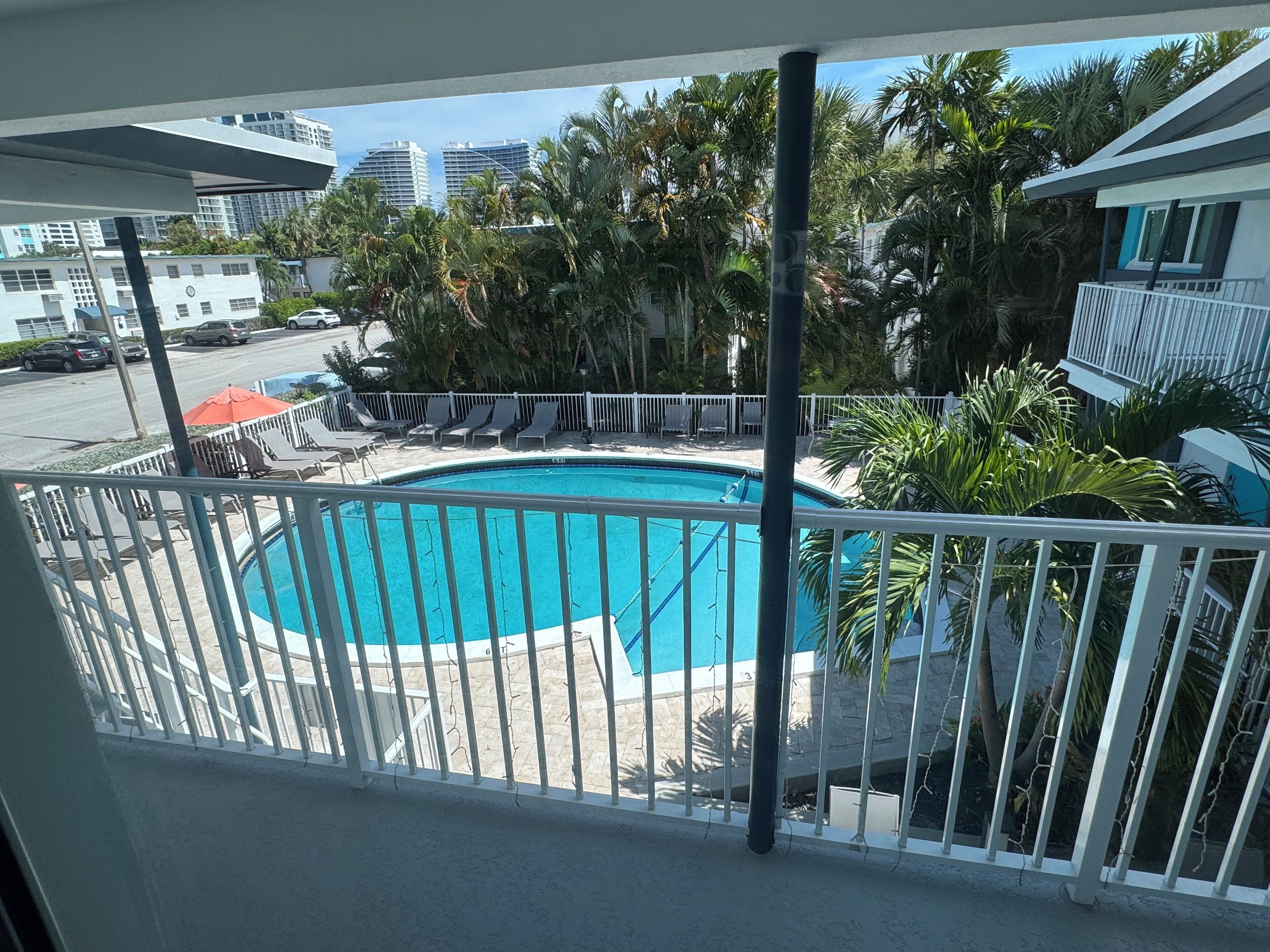 A pool area with a white fence, lounge chairs, and palm trees.