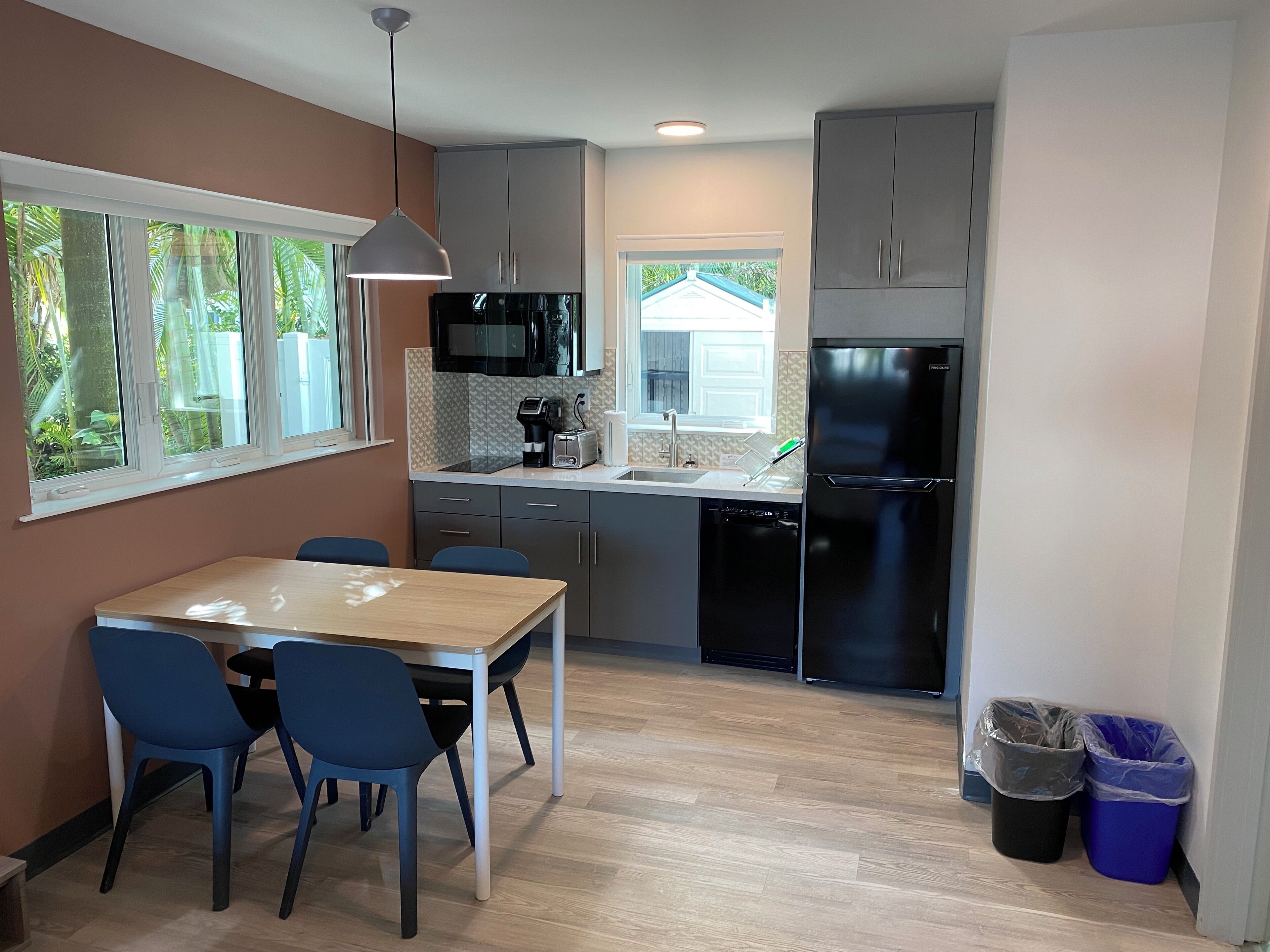 Eine moderne Küche mit Essbereich, ausgestattet mit einem Holztisch und blauen Stühlen, einem schwarzen Kühlschrank und einer Mikrowelle.