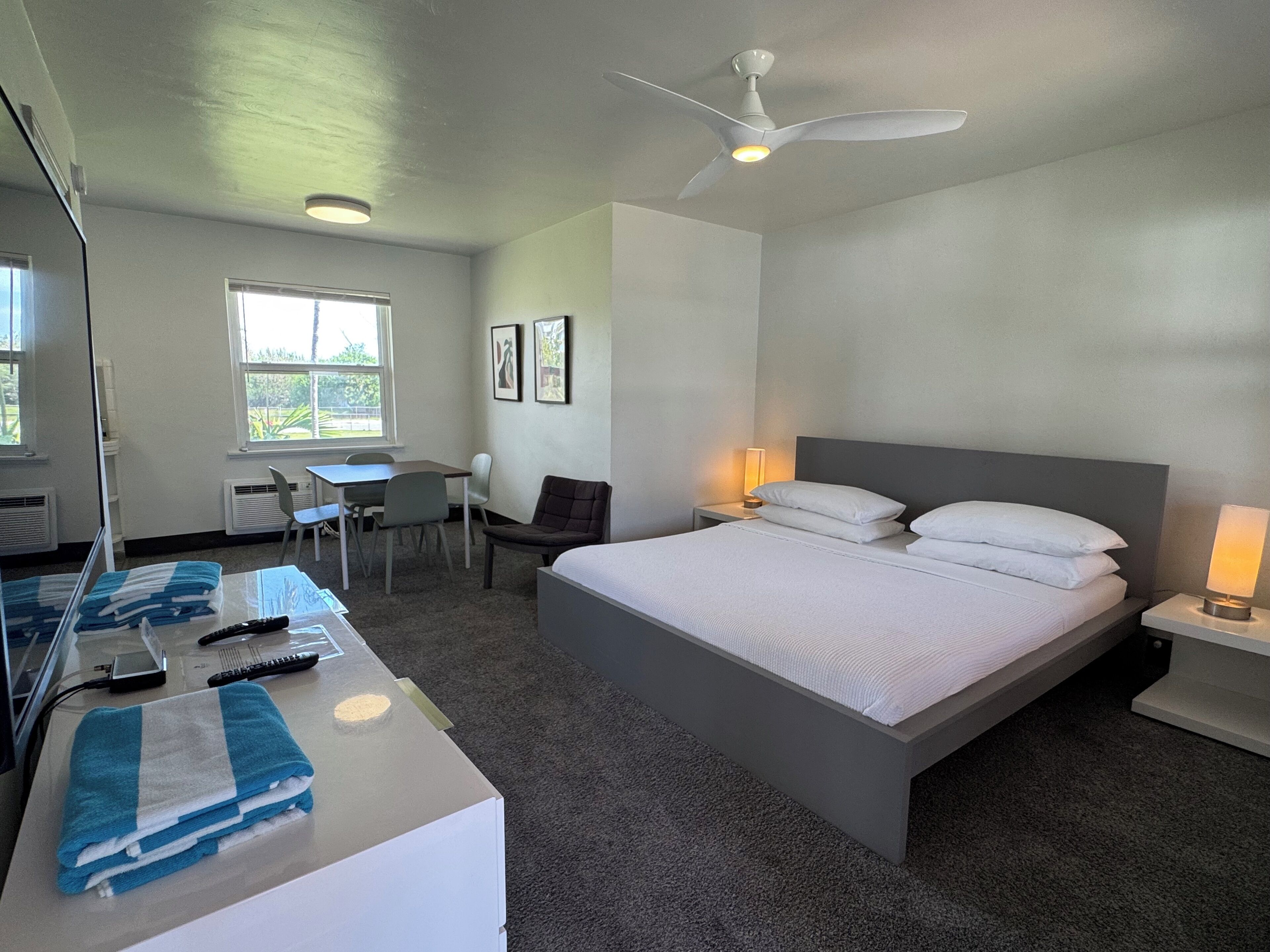 Una habitación de hotel con cama, mesitas de noche, escritorio, silla y ventilador de techo.