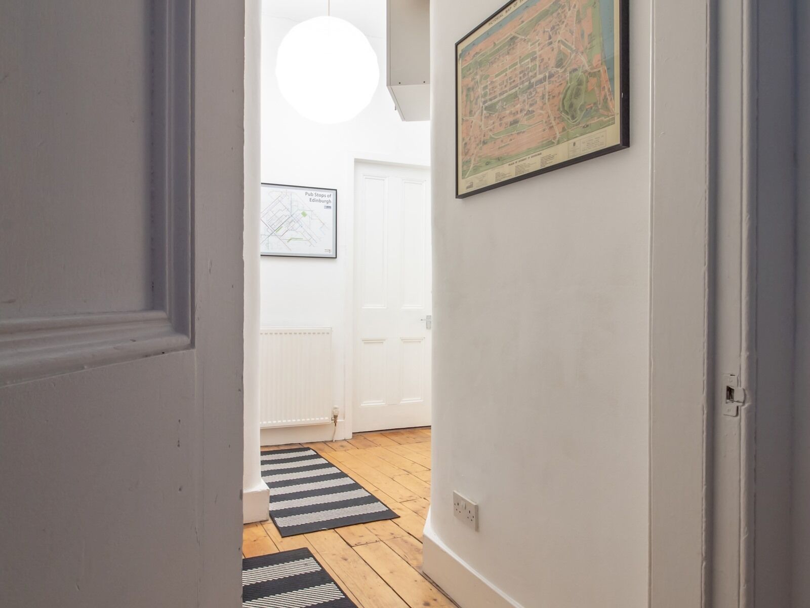 A hallway with a white door, a black and white striped rug, a framed map on the wall, and a white radiator.