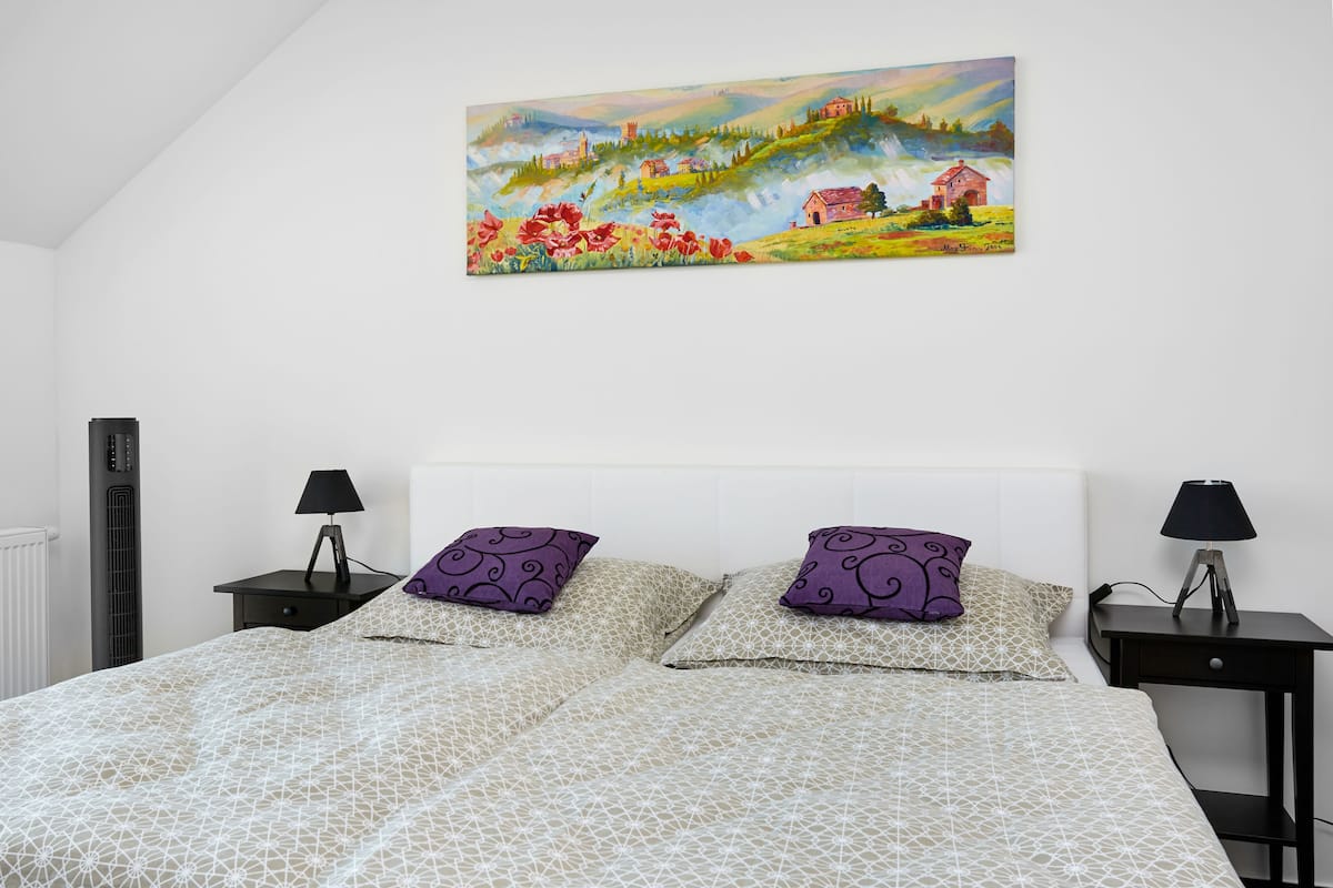 Un dormitorio con una cama, dos mesitas de noche, un cuadro y un radiador.