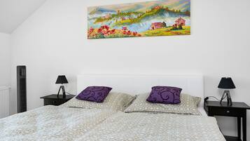 A bedroom with a bed, two nightstands, a painting, and a radiator.