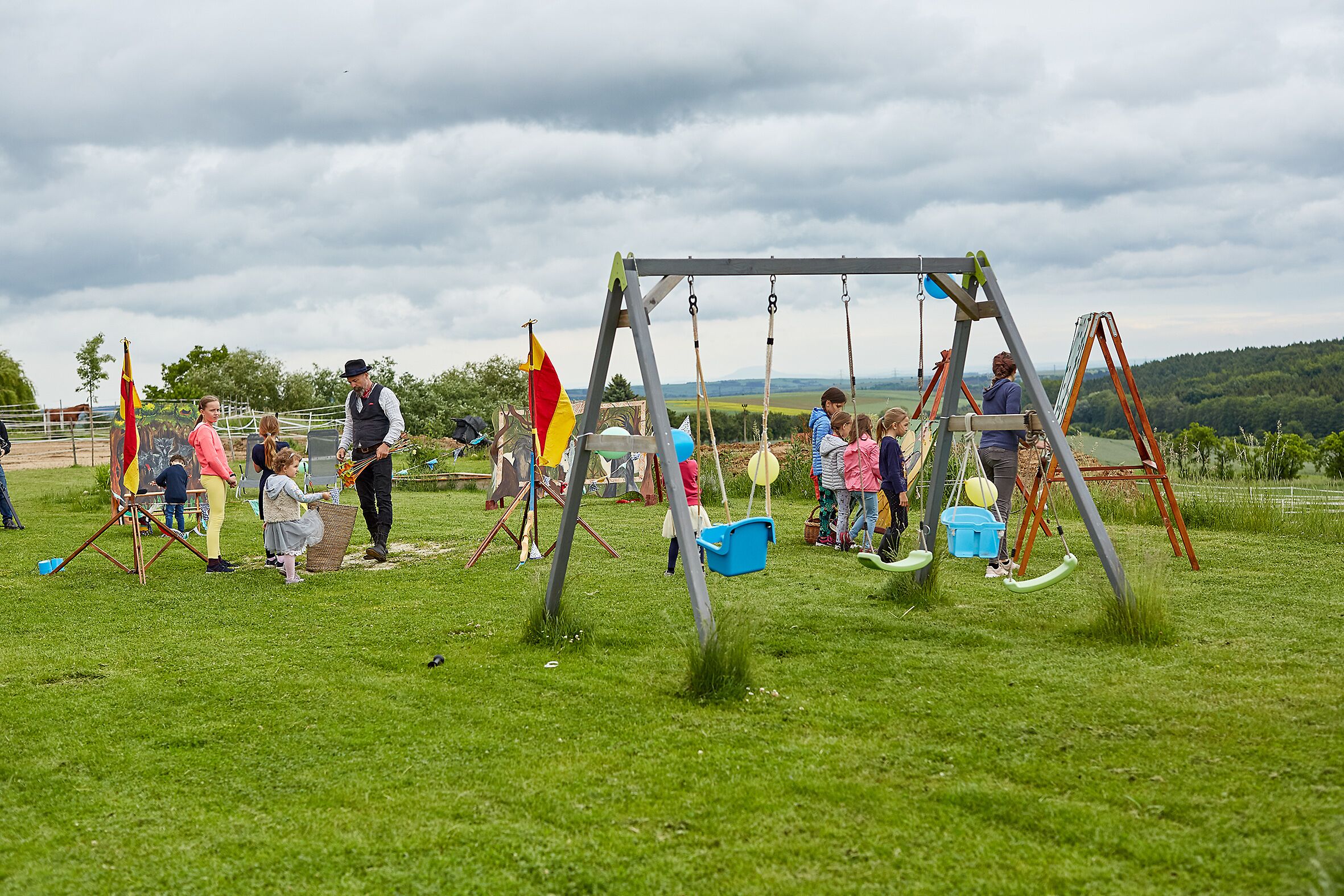 Un parque infantil con columpios y un tobogán, rodeado de un campo de césped y árboles.