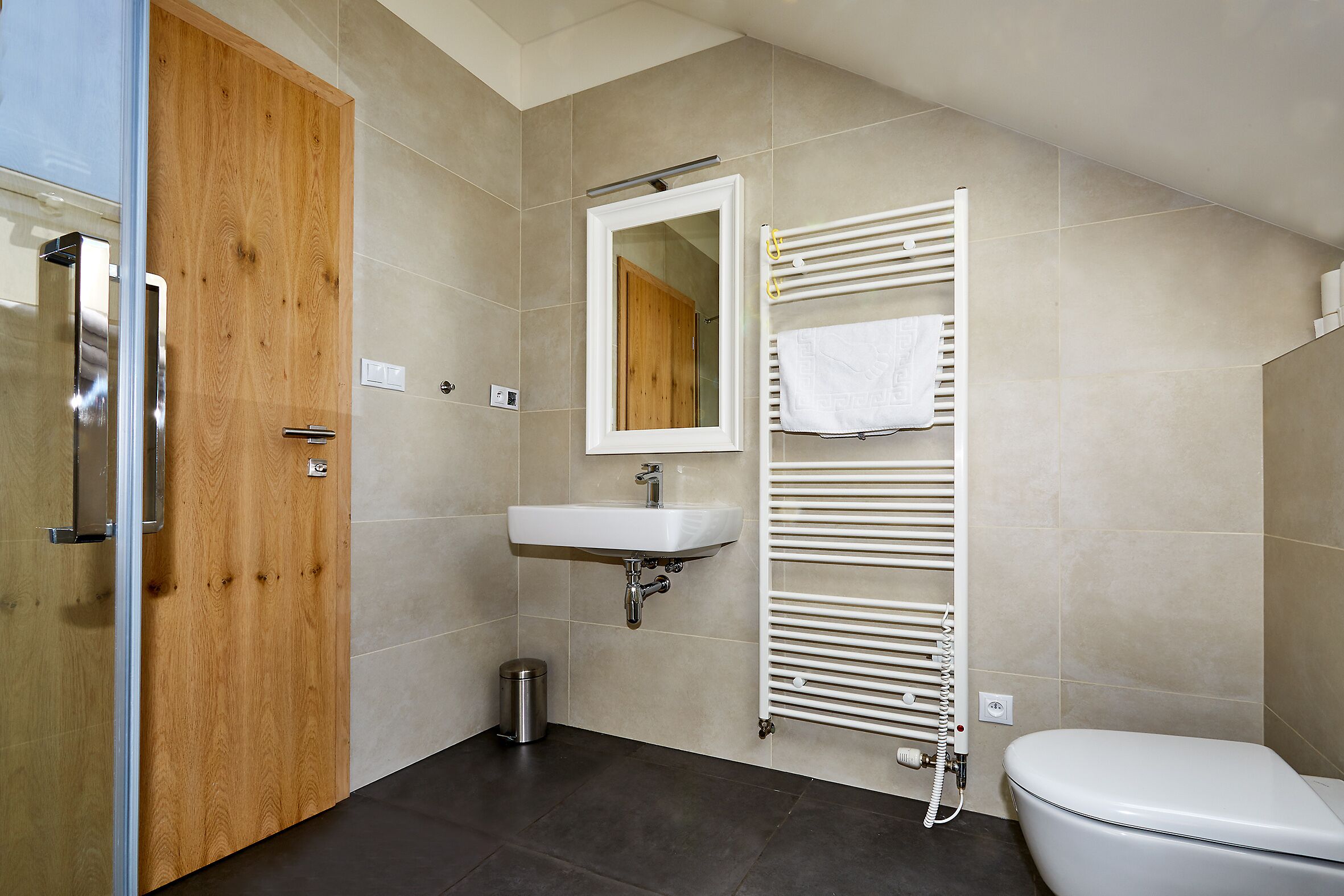 A modern bathroom with a wooden door, a white sink, a towel rack, and a toilet.