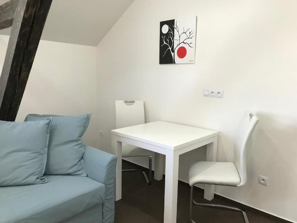 A room with a white table and two chairs, a light blue sofa, and a wall-mounted artwork.