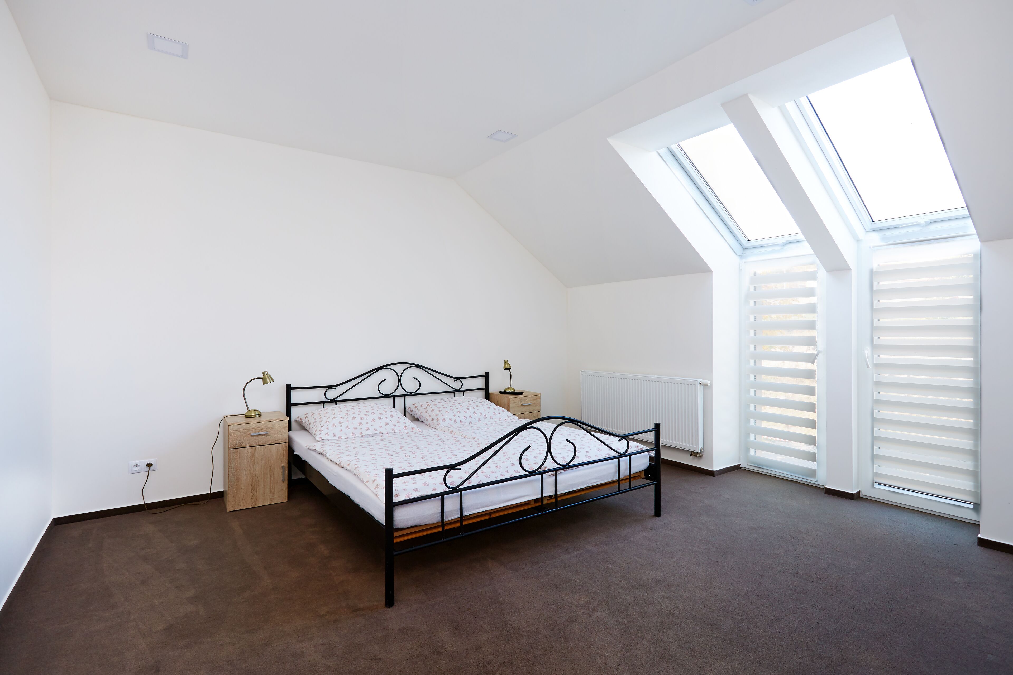 A bedroom with a bed, bedside tables, a radiator, and skylights.
