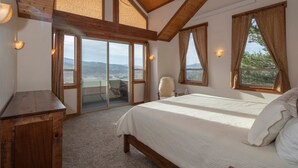 A bedroom with a large bed, wooden ceiling beams, a desk, and a view of the outdoors. - Alpine Recharge (Alpine)