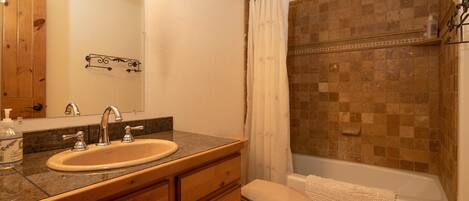 Un baño con lavabo, espejo, tocador de madera, inodoro y zona de ducha con pared de azulejos.