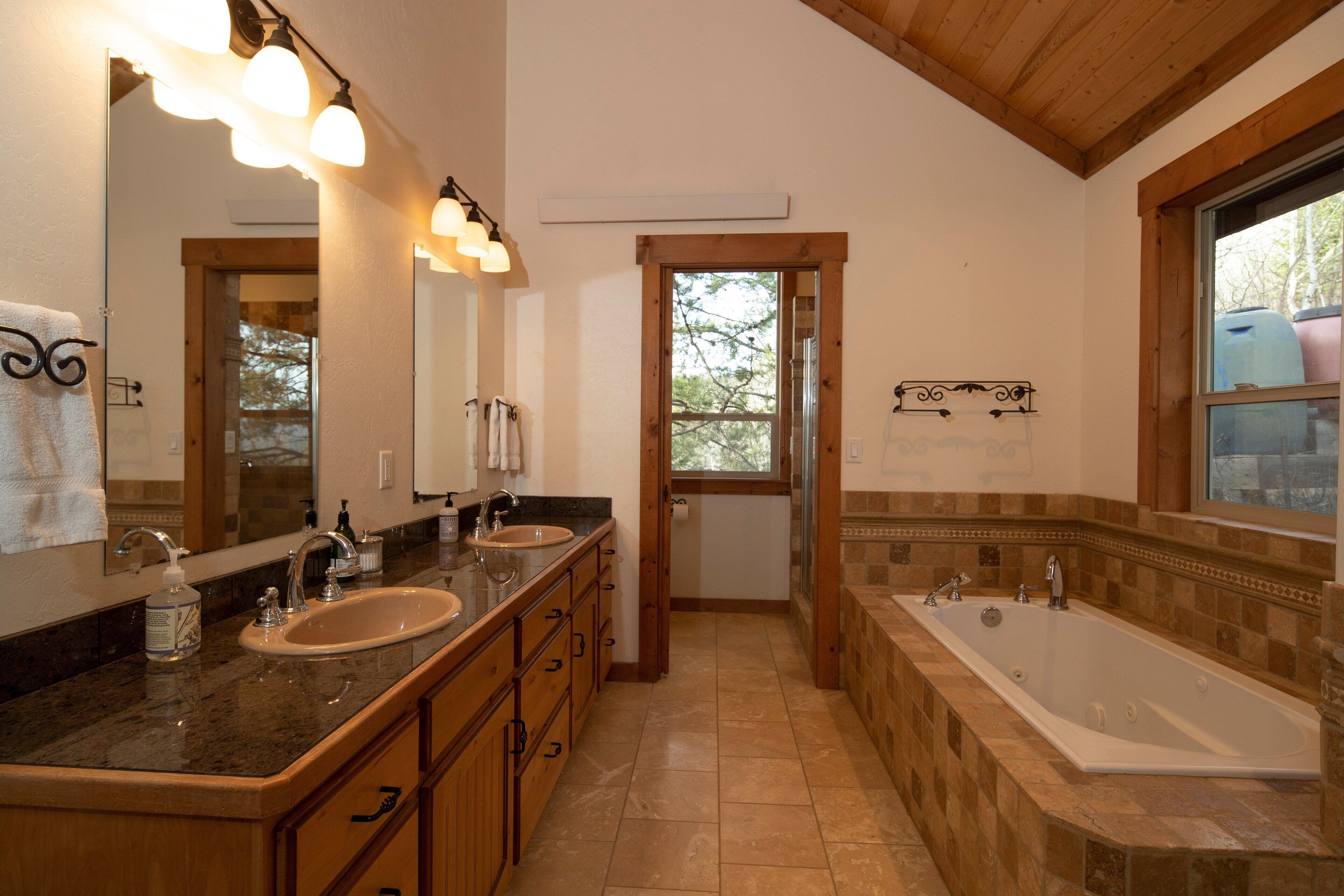 A bathroom with two sinks, a large bathtub, and a window with a view of trees.