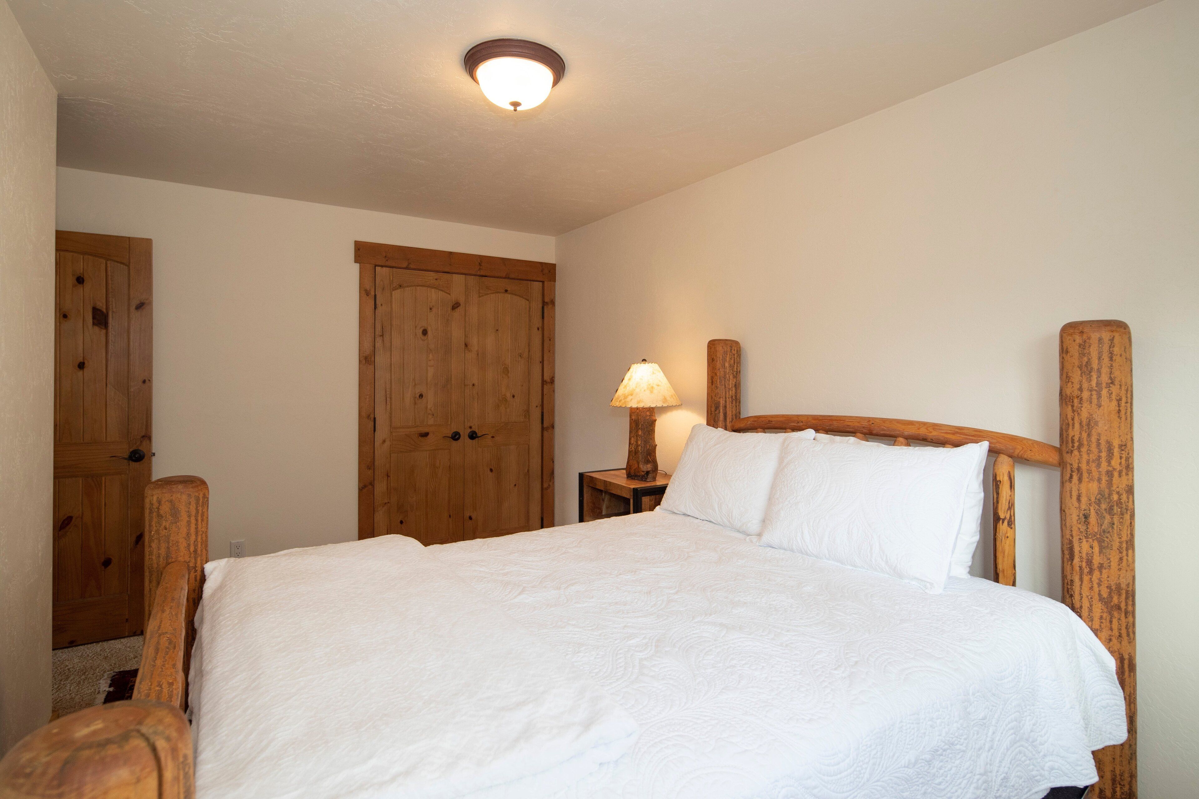 Camera da letto con una struttura letto in legno, biancheria da letto bianca, un comodino con una lampada e un'armadio in legno.
