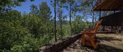 A rustic wooden bench by a stone wall overlooking a forested area with a clear blue sky.