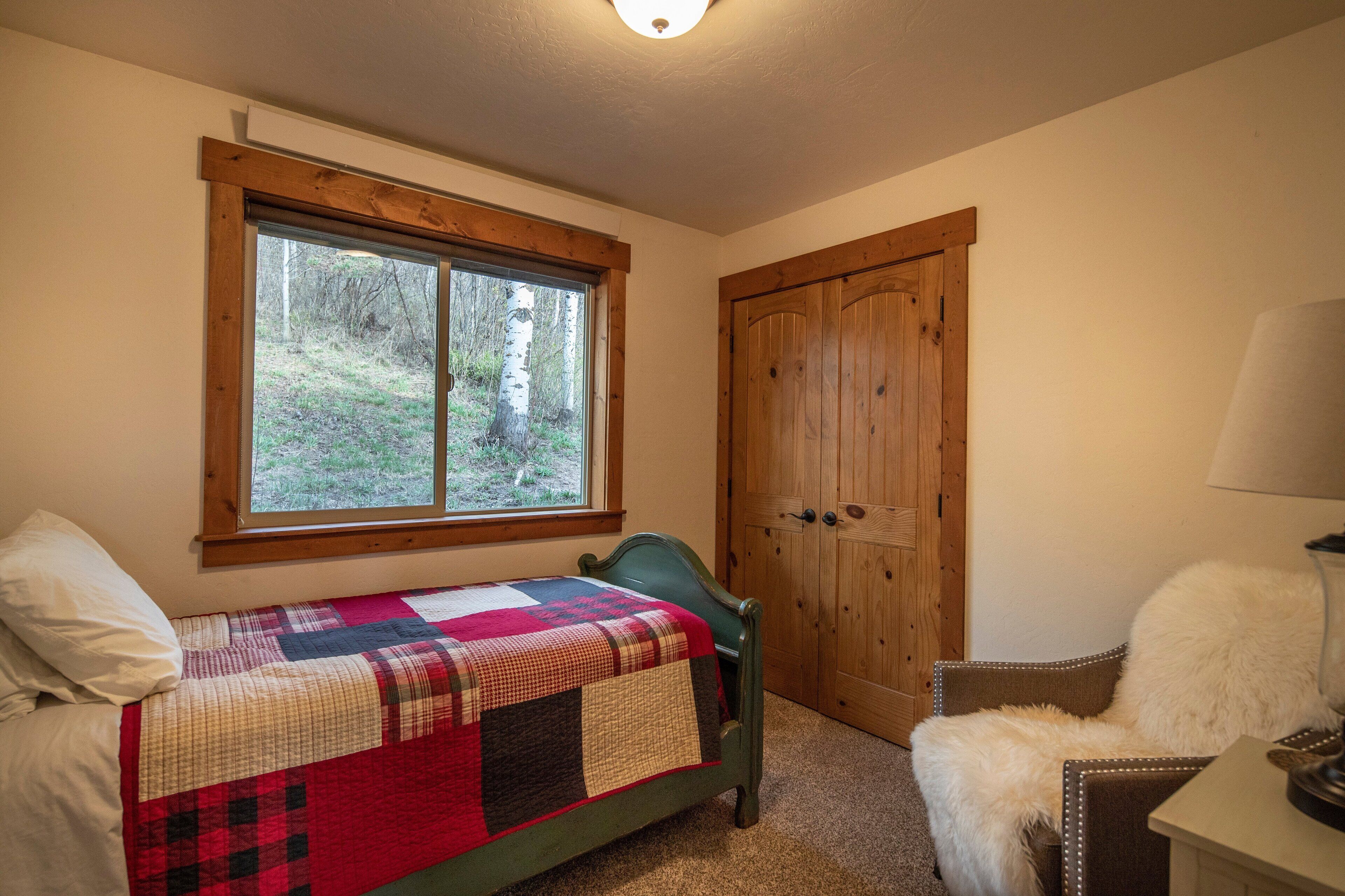 Una camera da letto con un letto, una sedia, un armadio in legno e una finestra vista alberi.