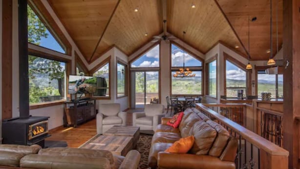 A spacious living area with a fireplace, leather sofa, and large windows offering views of the outdoors. - Alpine Recharge (Alpine)