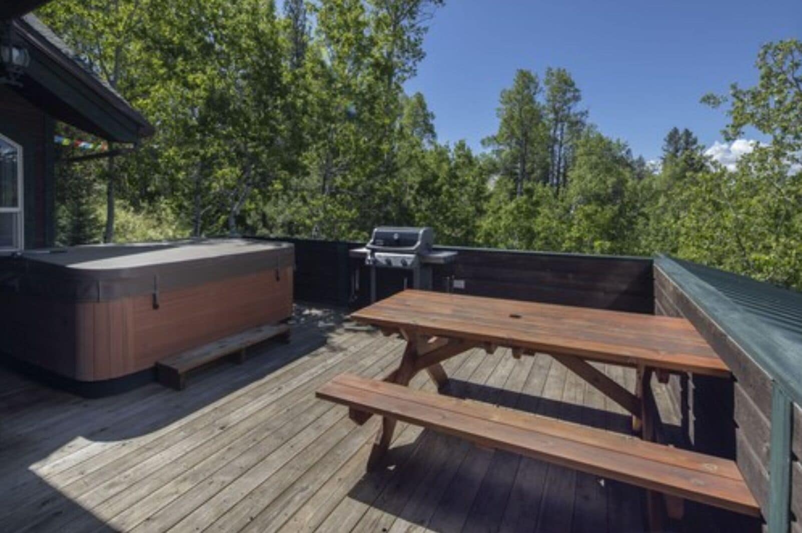 Une terrasse en bois équipée d’un jacuzzi, d’un barbecue et d’une table de pique-nique.