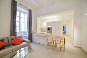 A modern living room with a glass coffee table, a sofa with red cushions, and a dining area with wooden chairs.