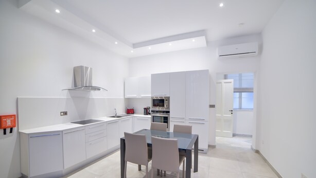 Una cocina moderna con armarios blancos, una mesa de comedor con sillas y un horno.
