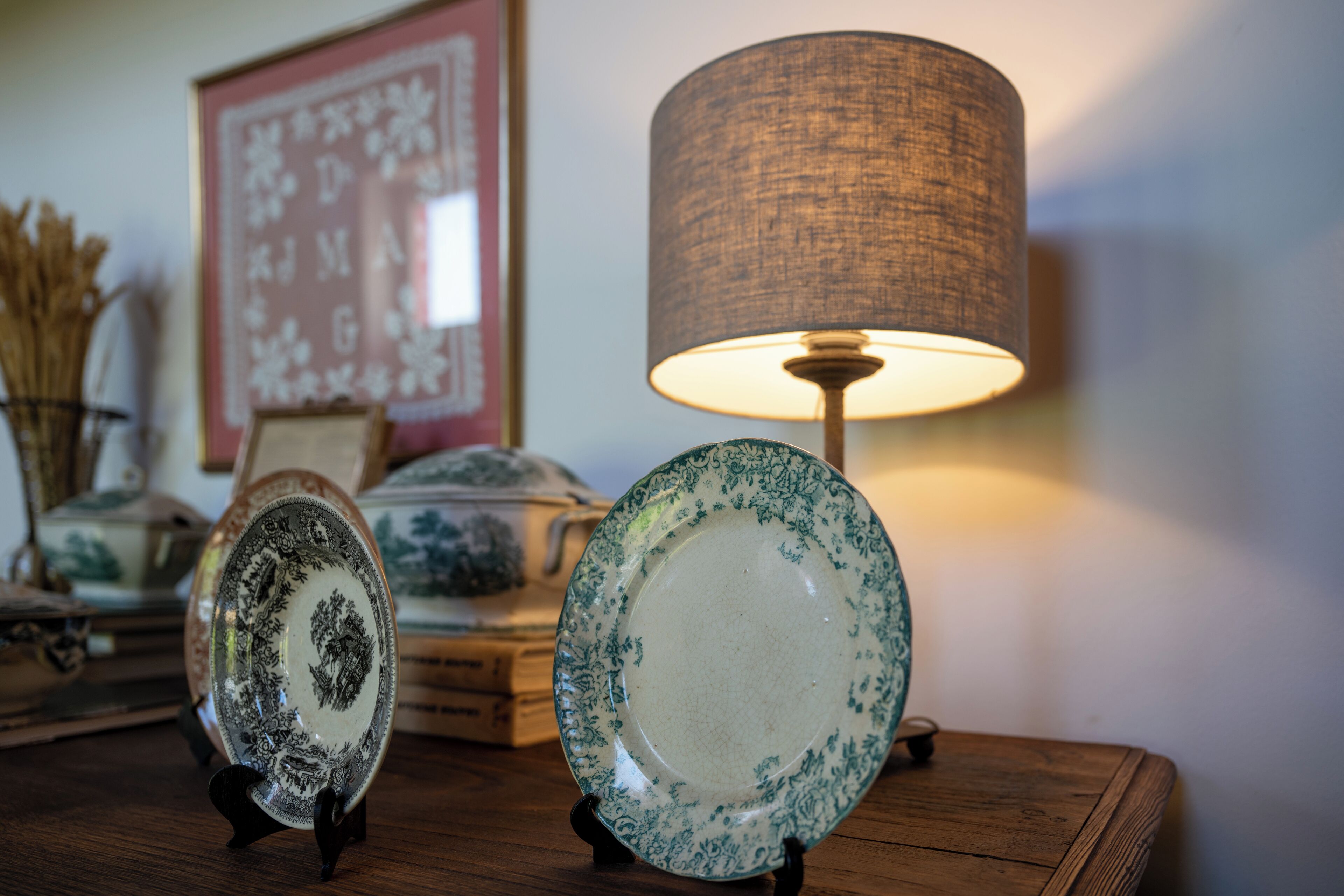 Twee keramieken borden op voetstukken, een lamp en een lijst met afbeelding op een houten tafel.