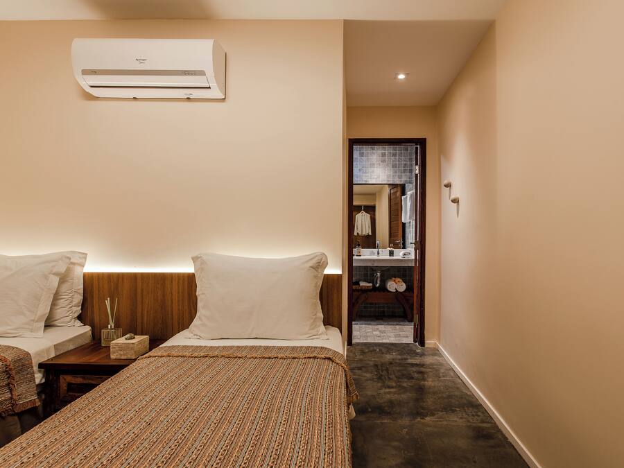 A hotel room with two beds, a wooden nightstand, a wall-mounted air conditioner, and a bathroom visible through an open door.