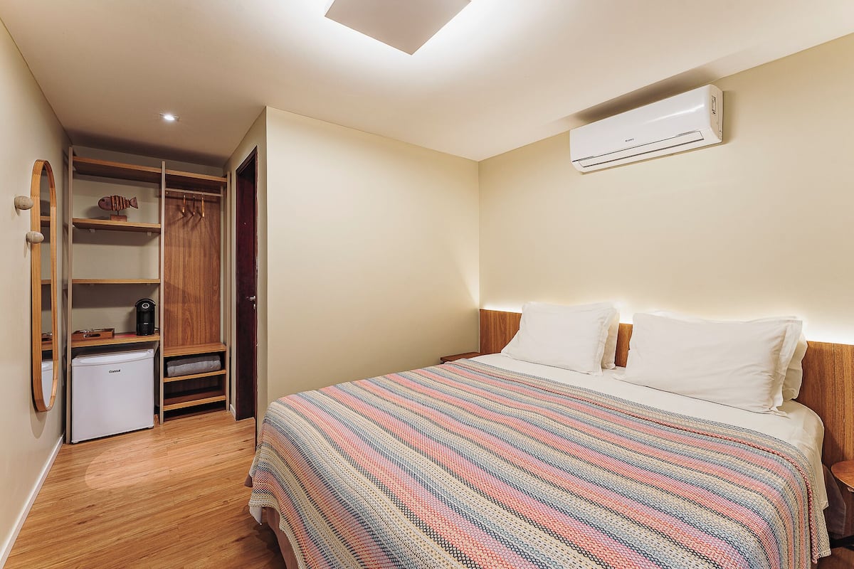 Ein Schlafzimmer mit einem Bett, einem Kleiderschrank, einem kleinen Kühlschrank und einer Klimaanlage.