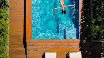Piscina com uma pessoa nadando, rodeada por um deck de madeira e vegetação.