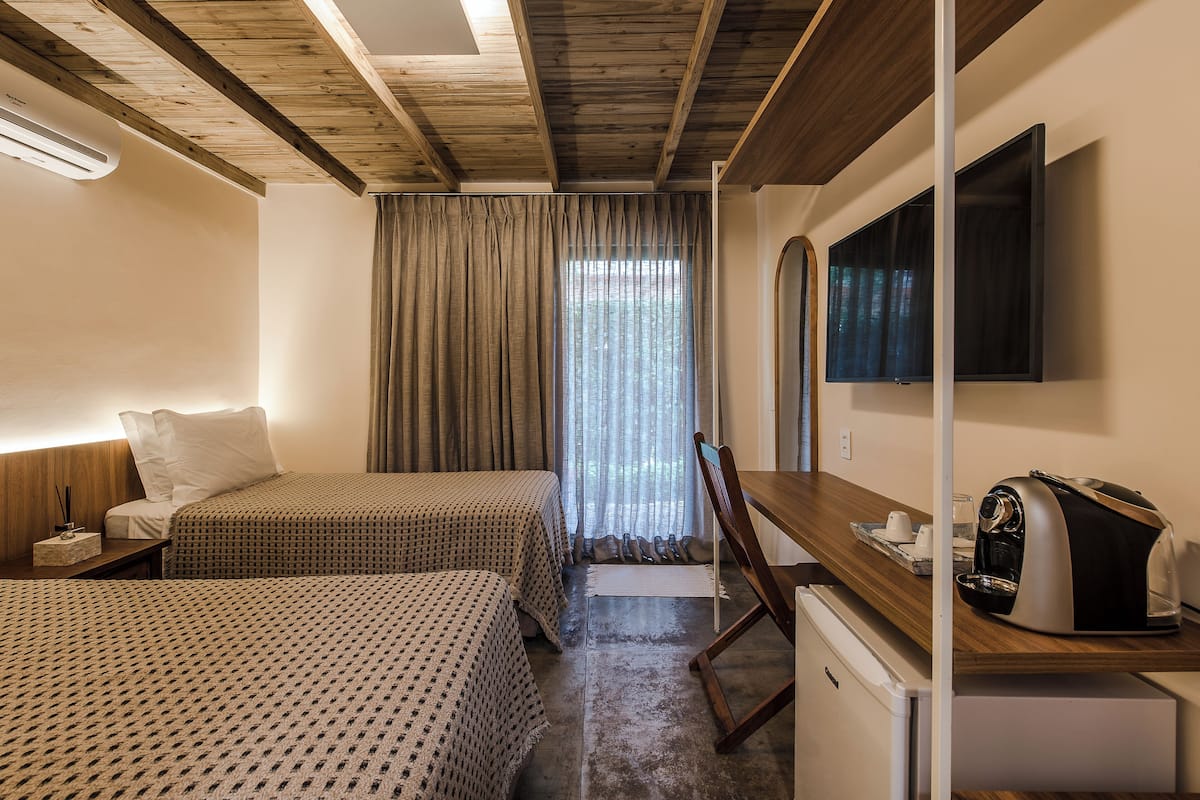 Ein Hotelzimmer mit zwei Betten, einem Schreibtisch mit Kaffeemaschine, einem Spiegel und einem Fenster mit Vorhängen.