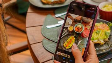 Una persona sosteniendo un teléfono inteligente con una aplicación de fotografía de comida abierta, mostrando varios platos.