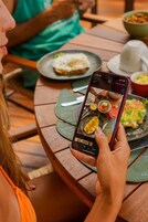 Una persona sosteniendo un teléfono inteligente con una aplicación de fotografía de comida abierta, mostrando varios platos.