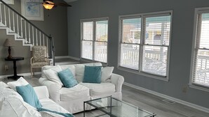 A spacious living room with a white sofa set, a glass coffee table, and a ceiling fan. - Ocean Retreat with Private Beach Access (Kure Beach)