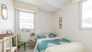 A bedroom with a bed, a chair, a small table, a lamp, a window, and a mirror.