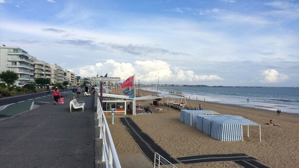 A beach with a promenade, beach umbrellas, and a flag.