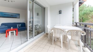 A balcony with a white table and chairs, a red table, and a blue sofa with a cushion.
