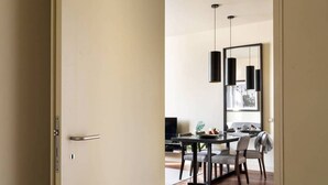 A modern dining area with a minimalist design, featuring a dark-toned table and chairs, a pendant light fixture, and a large mirror above the table. - JOIVY Urban 2BR Apt w/ Park view, in Cais do Sodré (Lisboa)