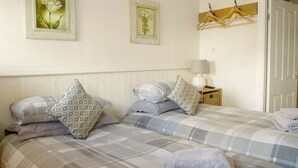 Ein Schlafzimmer mit zwei Betten, jeweils mit gemusterten Bettbezügen und Kissen, einem Nachttisch mit Lampe sowie zwei gerahmten floralen Bildern an der Wand.