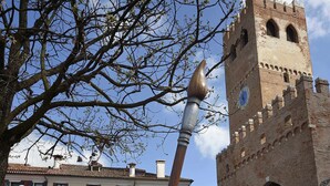 Pyöreä puupöytä, jonka päällä on värikkäitä kukkakimppuja, ja taustalla historiallinen rakennus, jossa on kellotorni.