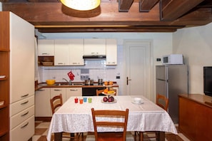 Une cuisine compacte avec des meubles blancs, un plafond en bois et une table à manger recouverte d’une nappe blanche.